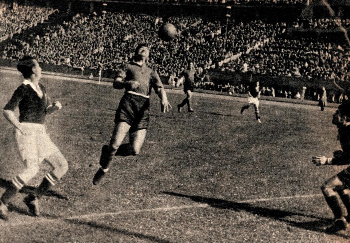 Imagen iQué demostración de "limpieza" en todos sus aspectos nos da esta foto! Sin alambrados altos como previsión; orden en la ropa de los jugadores y en las tribunas. Un solo particular al costado de la cancha, el césped parejo y bien cortadito. Uno se imagina el sol, unía pelota nueva iY una invitación a correr, a jugar!.. 