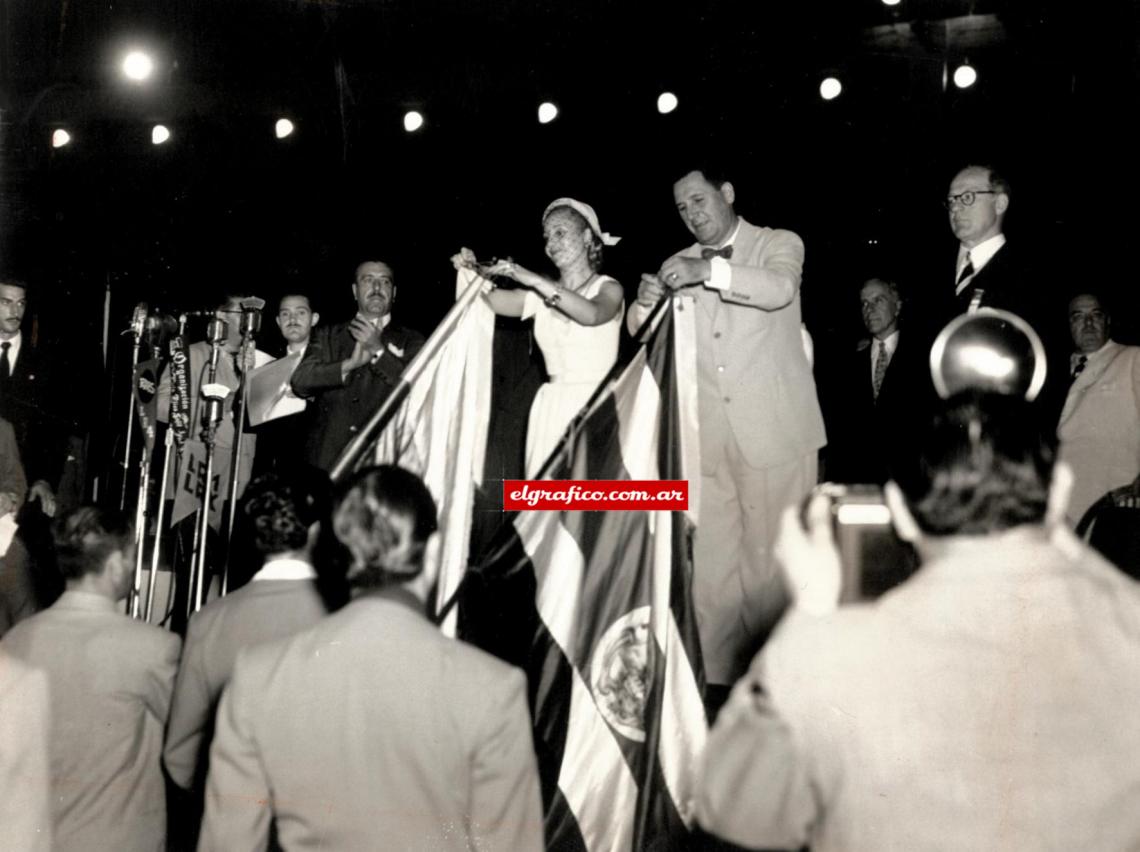 Imagen Juegos Panamericanos. Buenos Aires 1951. El presidente de la República y su señora esposa en una significativa ceremonia de fraternidad, proceden a enlazar cintas con los colores argentinos en las banderas de todos los países concurrentes. 