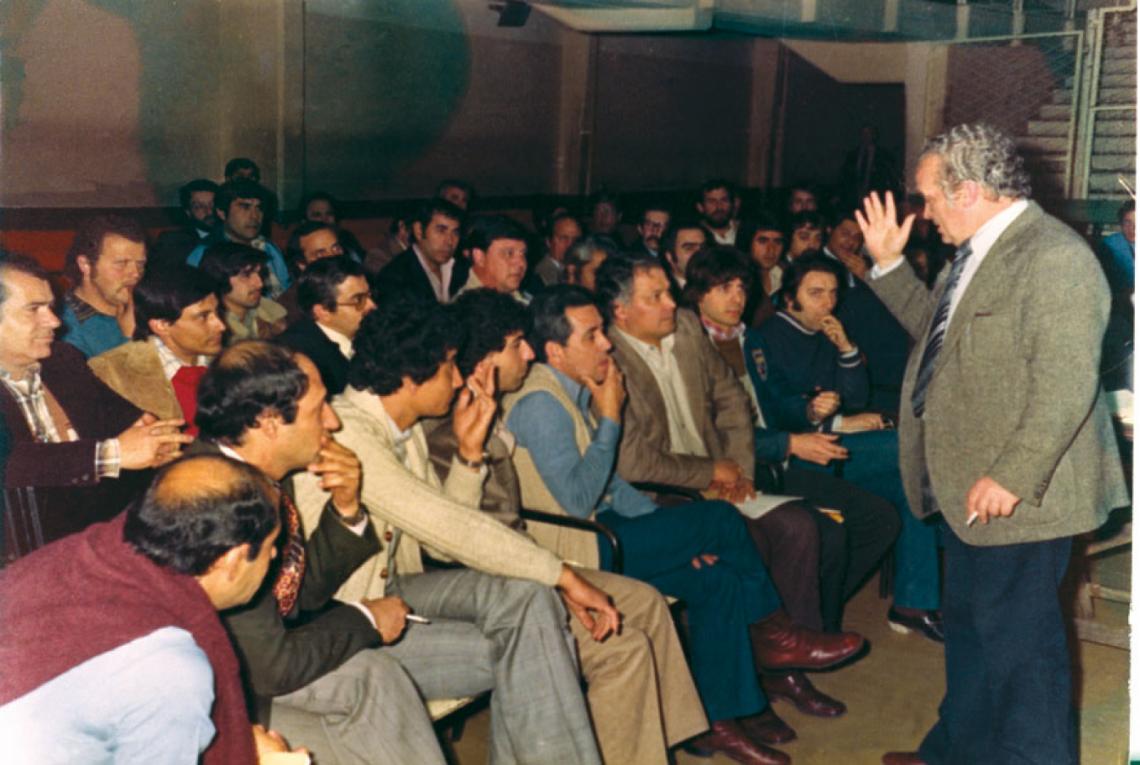 Imagen ESTUDIANDO. Ramón con las piernas cruzadas y un saco beige, recibiendo clases de un grande, José González.