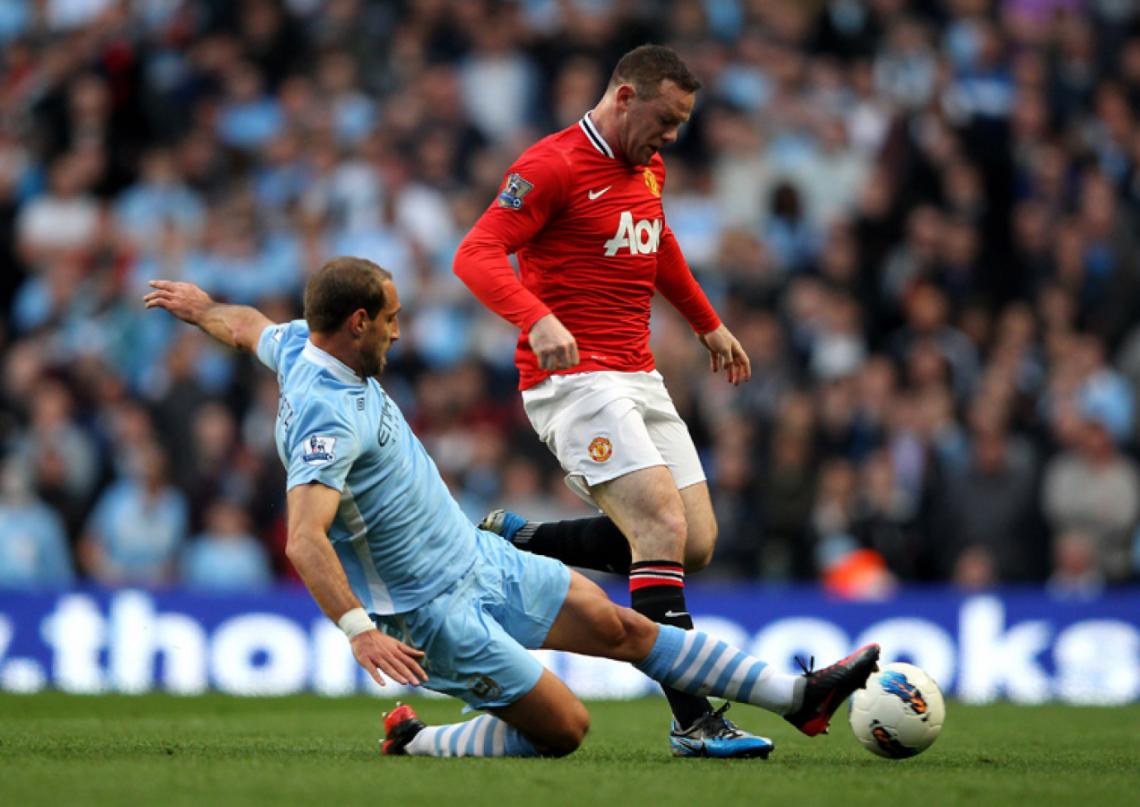 Imagen AL PISO. Zabaleta así también juega. Wayne Rooney lo sufre en el clásico de Manchester: City vs United.