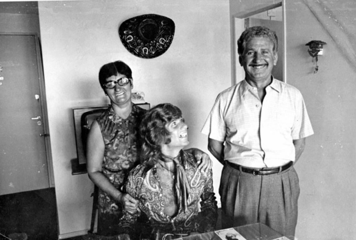 CON LOOK PSICODELICO, patillas y pelo largo, una postal de época con sus padres.