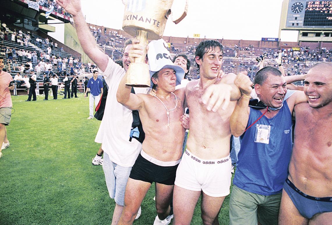Imagen La vuelta olímpica por la que Racing esperó 35 años: el 27 de diciembre 2001, en Liniers, tras igualar 1-1 con Vélez. Celebra abrazado con Arano y Vitali. Milito, Maciel y Vitali fueron los únicos con asistencia perfecta (19 partidos).