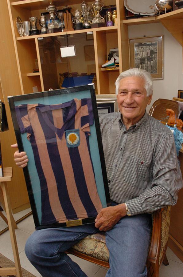 Imagen En uno de los rincones de su casa, rodeado de fotos, trofeos y distinciones. Aquí, mostrando la camiseta que usó durante los Torneos Evita, una reliquia que conserva con orgullo.