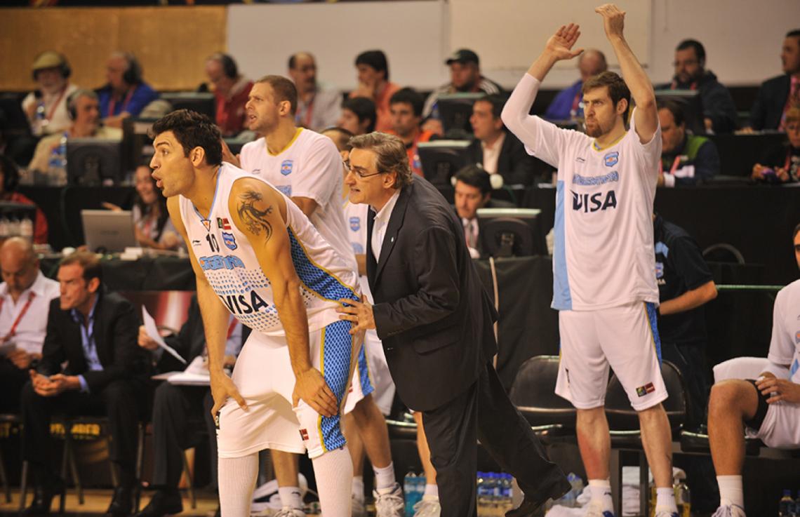 Imagen Lamas espía por detrás de Carlos Delfino, y Andrés Nocioni aplaude. Fue en su segunda etapa al frente de la Selección (2011-14).