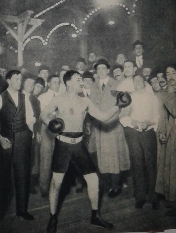 Imagen Aquí vemos a Alberto Mongiardini en 1912, cuando al vencer a González Acha se clasificó campeón de peso welter y obtuvo en premio el cinturón que luce, donado por el Dr. Pirovano. A espaldas de Mongiardini está su hermano Rodolfo. 
