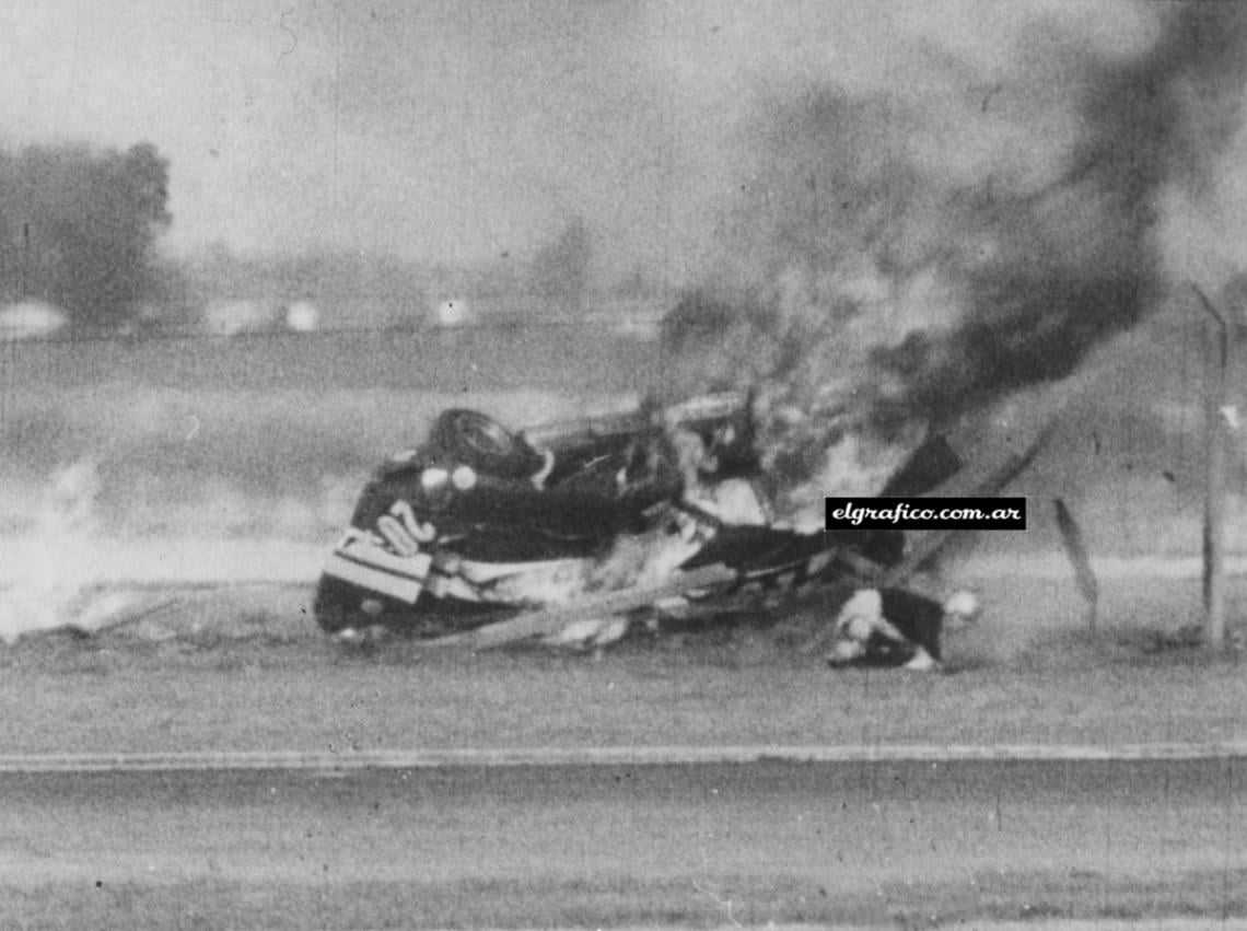 El piloto, arrodillado en el pasto, hace esfuerzos por incorporarse. A escasos dos metros suyos, el auto sigue ardiendo intensamente.